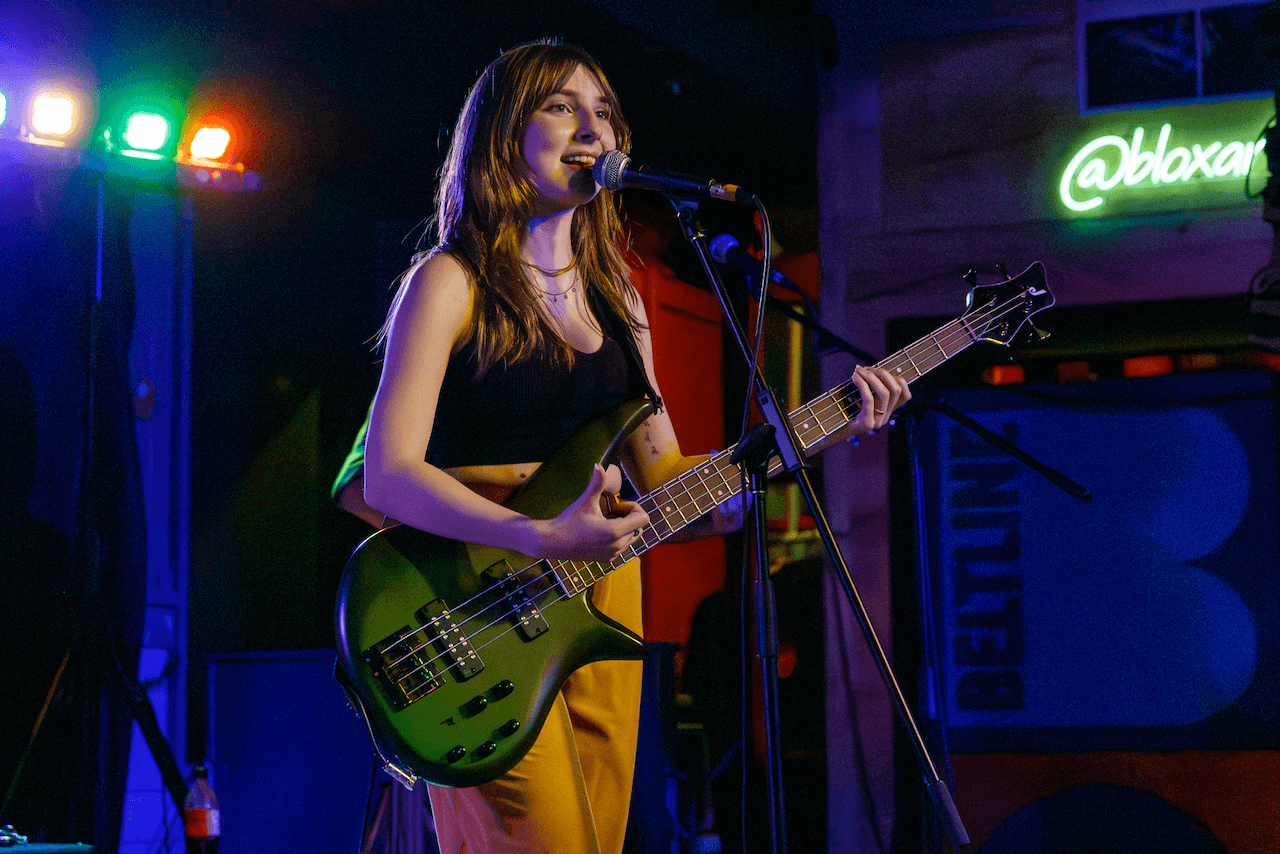 Tori Morley singing and playing bass on stage under colorful lights.