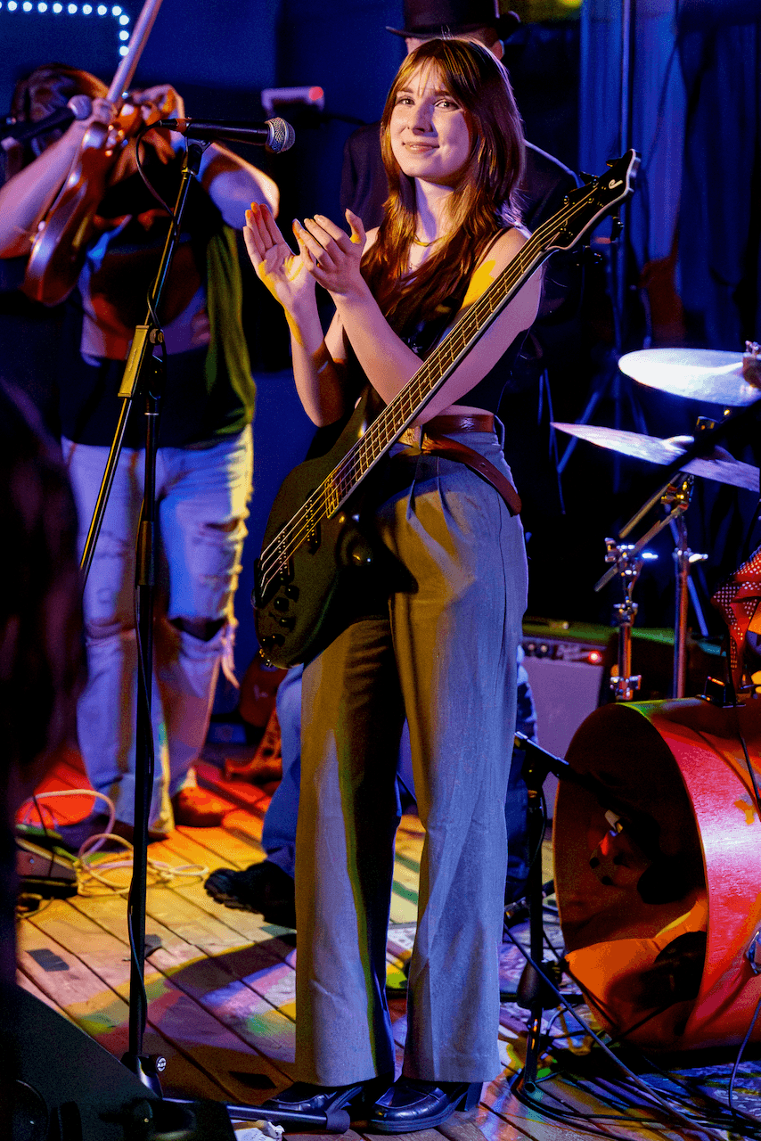Tori Morley on stage after a set, applauding with bass in hand.